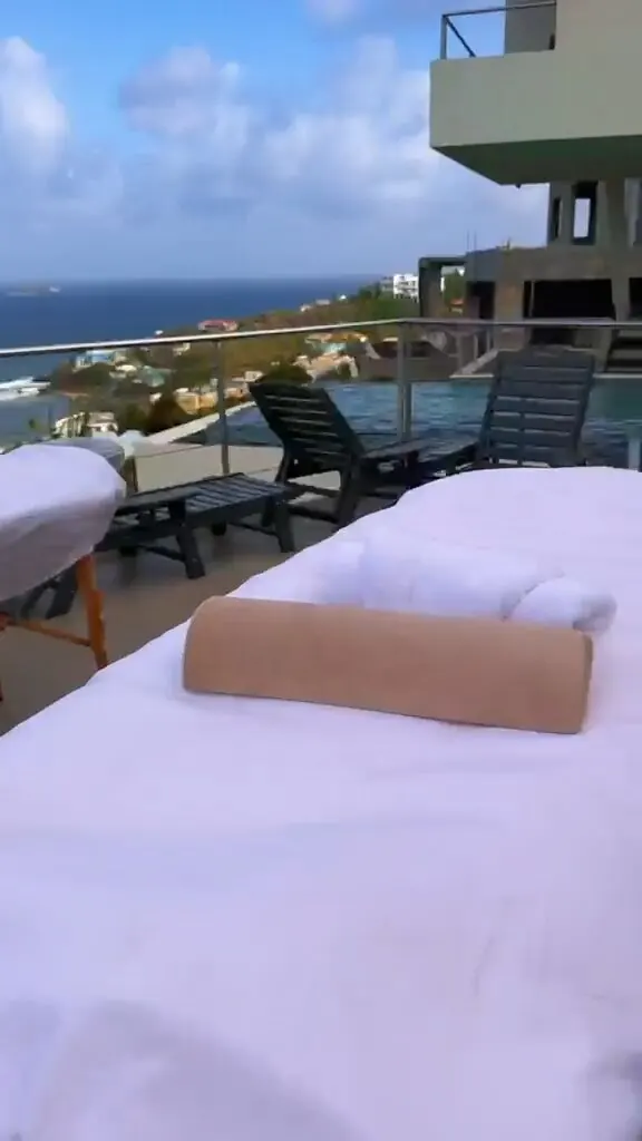 Massage table set up on a rooftop terrace with lounge chairs, a pool edge, and an ocean view