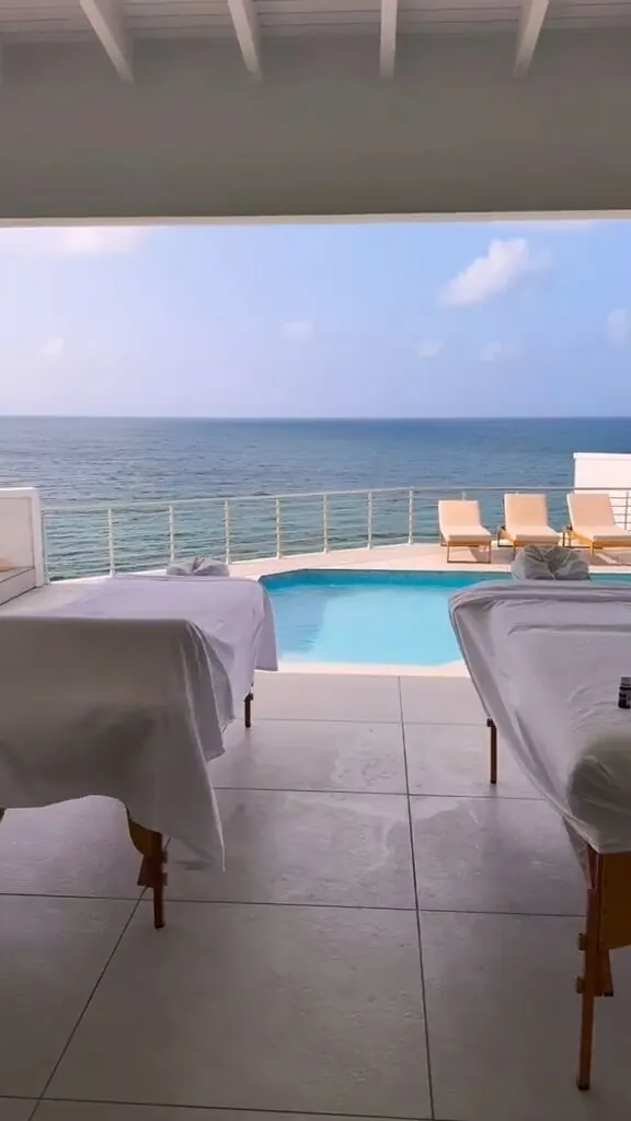 Two massage tables set up side by side under a covered pergola beside an infinity pool overlooking the ocean
