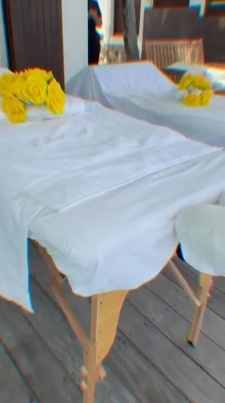 Massage tables set with fresh yellow flowers and rolled towels on a wooden deck beside the pool