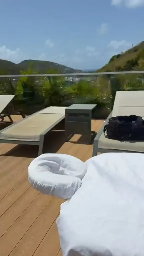 Lounge chairs and a massage table set up on a hillside villa deck overlooking the hills and distant ocean