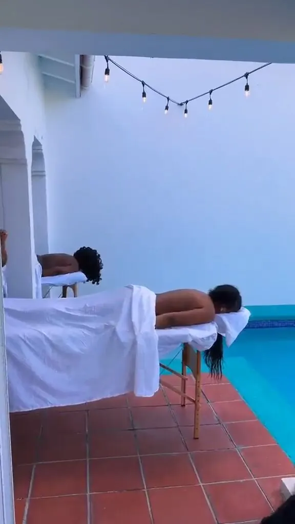 Two guests relaxing during an evening poolside massage under string lights